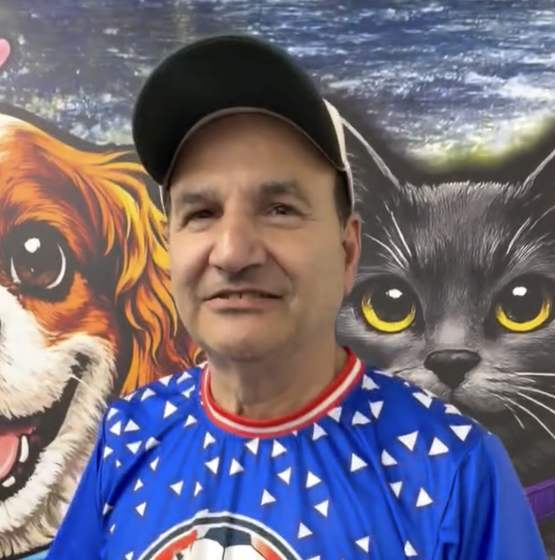 George Diguido, owner of NYC Pet, standing in the store in front of a painted mural of a dog and a cat