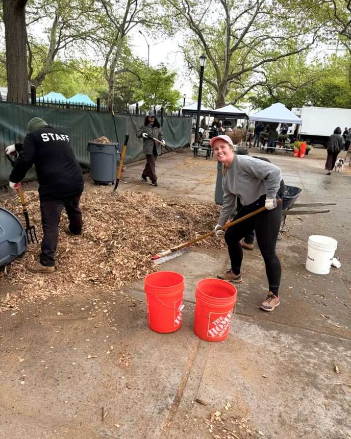 Volunteers with rakes and buckets spreading fresh mulch across a dog run